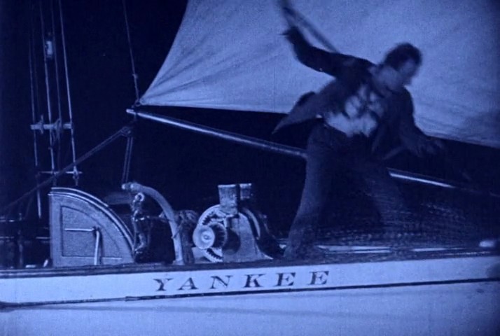 Frame from Wild Oranges showing YANKEE on the bow name board as an actor works on deck