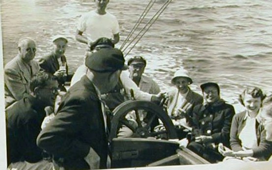 Ship's company gathered around Yankee's wheel at sea — a photograph pasted into the schooner's own logbook